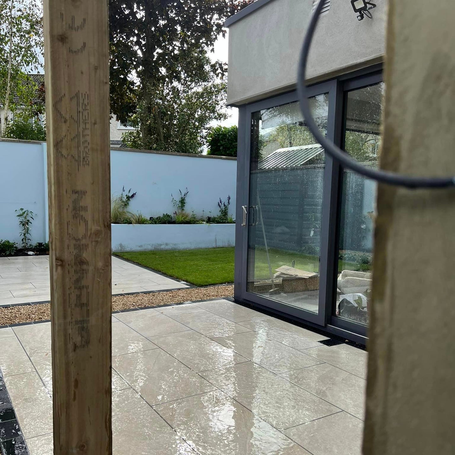 Another view of small patio area looking out on blue planter wall and small patch of grass. Paving is Cream Twice Qz Range Porcelain Paving Tiles. 