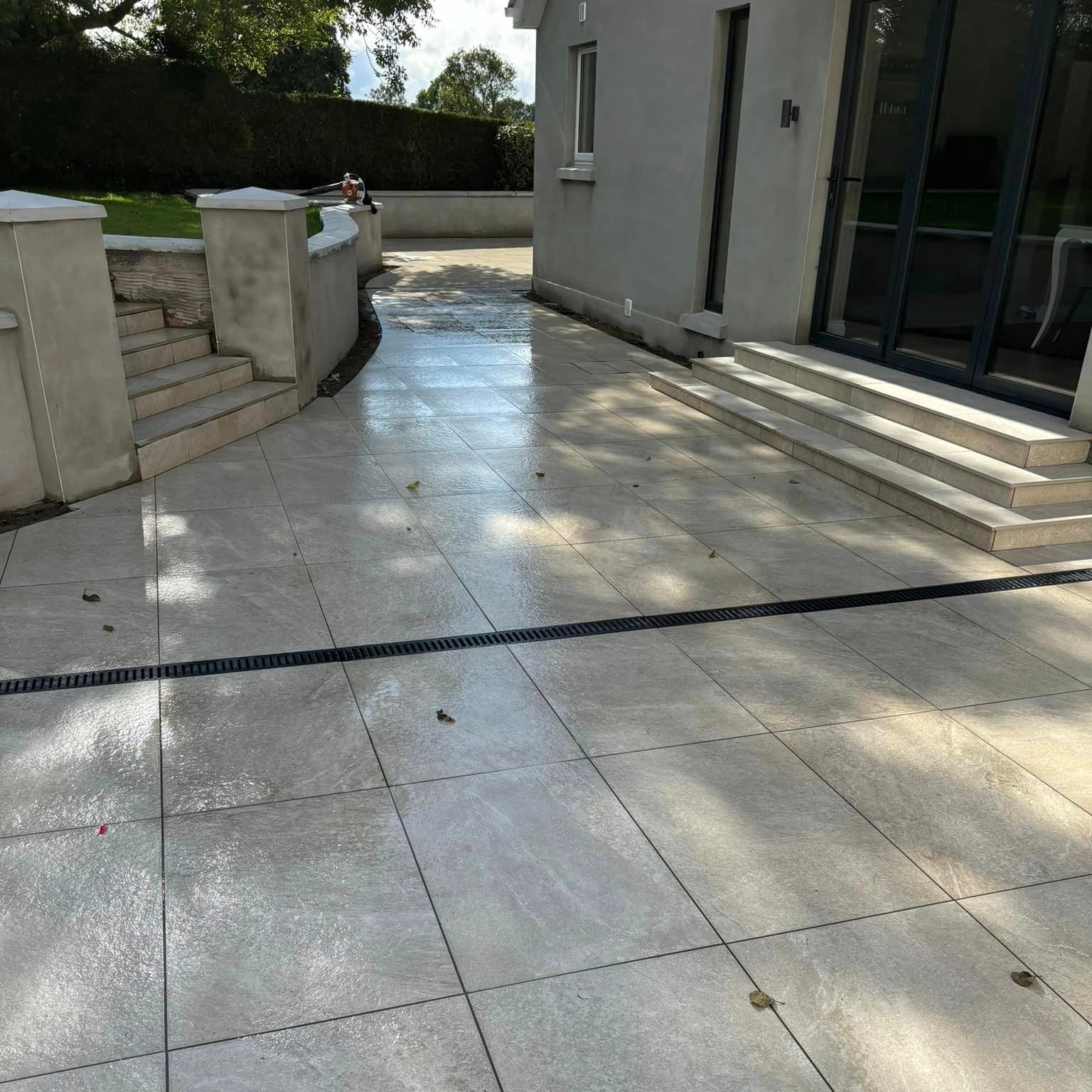 Modern patio area with steps up to garden and patio doors. Paving is Cream Twice Qz Range Porcelain Paving Tiles. 