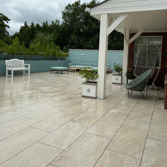 Large patio area with white canopy and blue wall and trees in the background. Paving is Cream Twice Qz Range Porcelain Paving Tiles. 