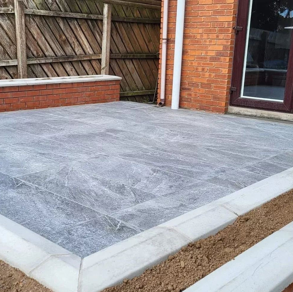Small patio area with red brick house and wall in the background. Paving is Dark Twice Qz Range Porcelain Paving Tiles. 