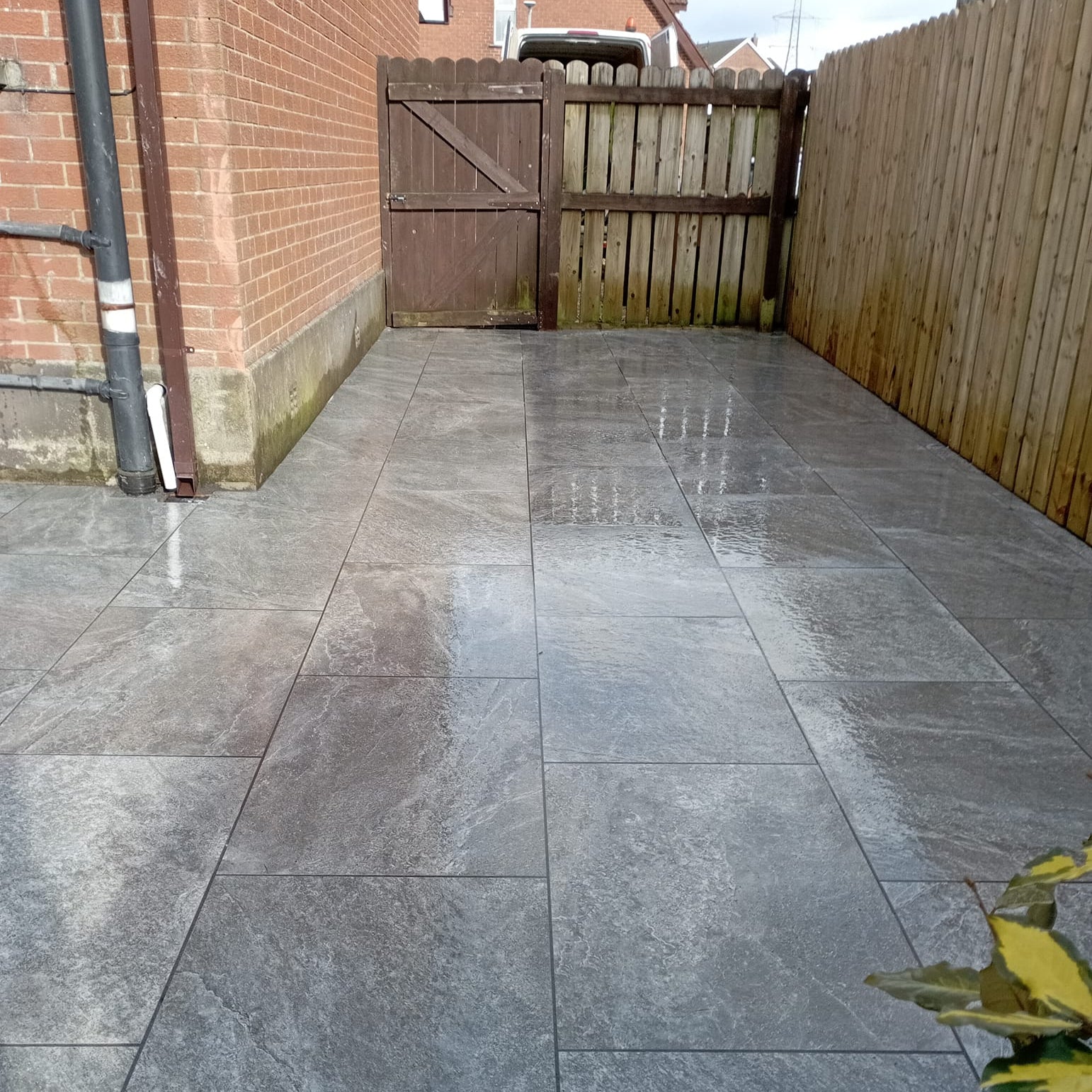 patio area of a red brick house surrounded by large wooden fence. Paving is Dark Twice Qz Range Porcelain Paving Tiles. 