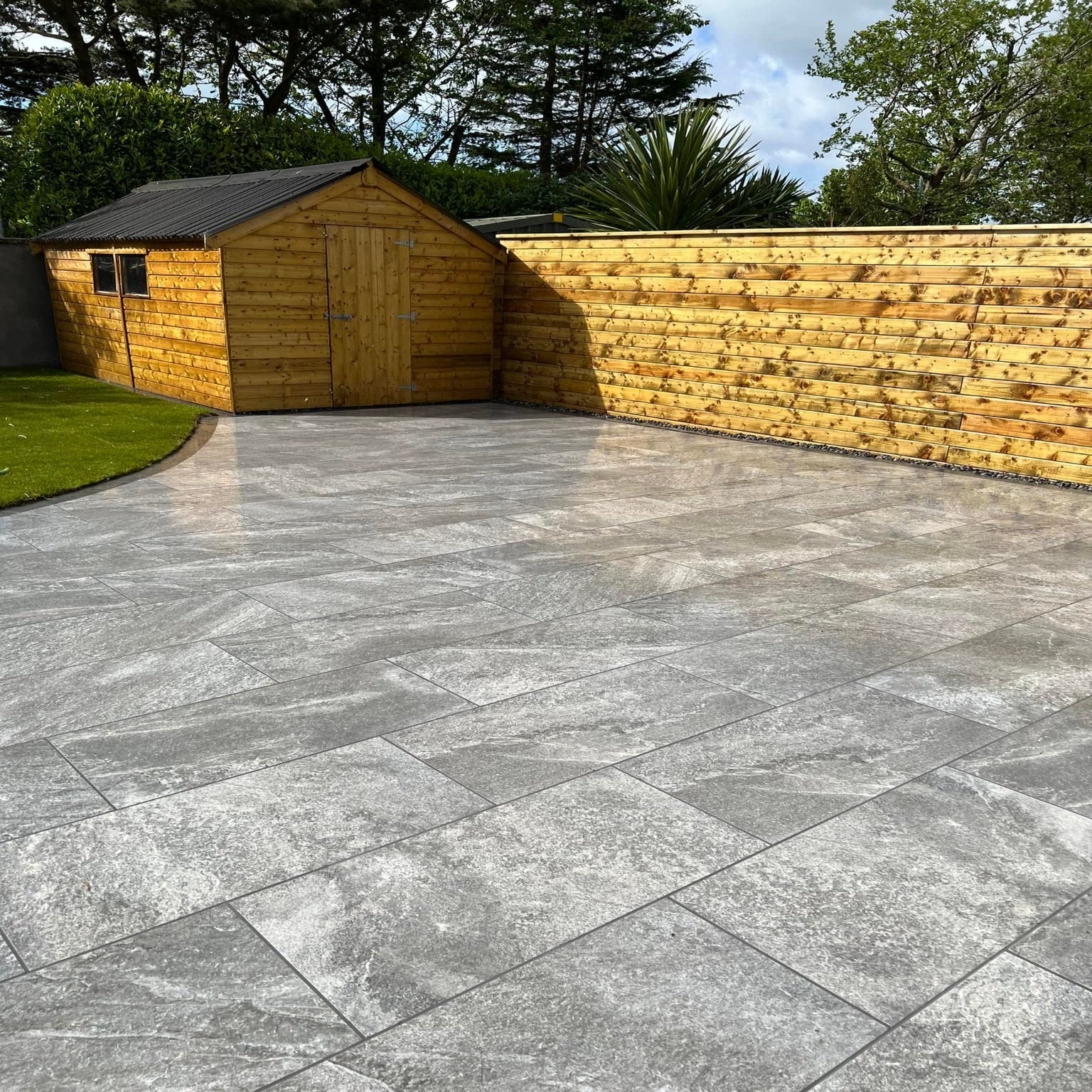 Large patio with garden shed and wooden fence. Paving is Dark Twice Qz Range Porcelain Paving Tiles. 