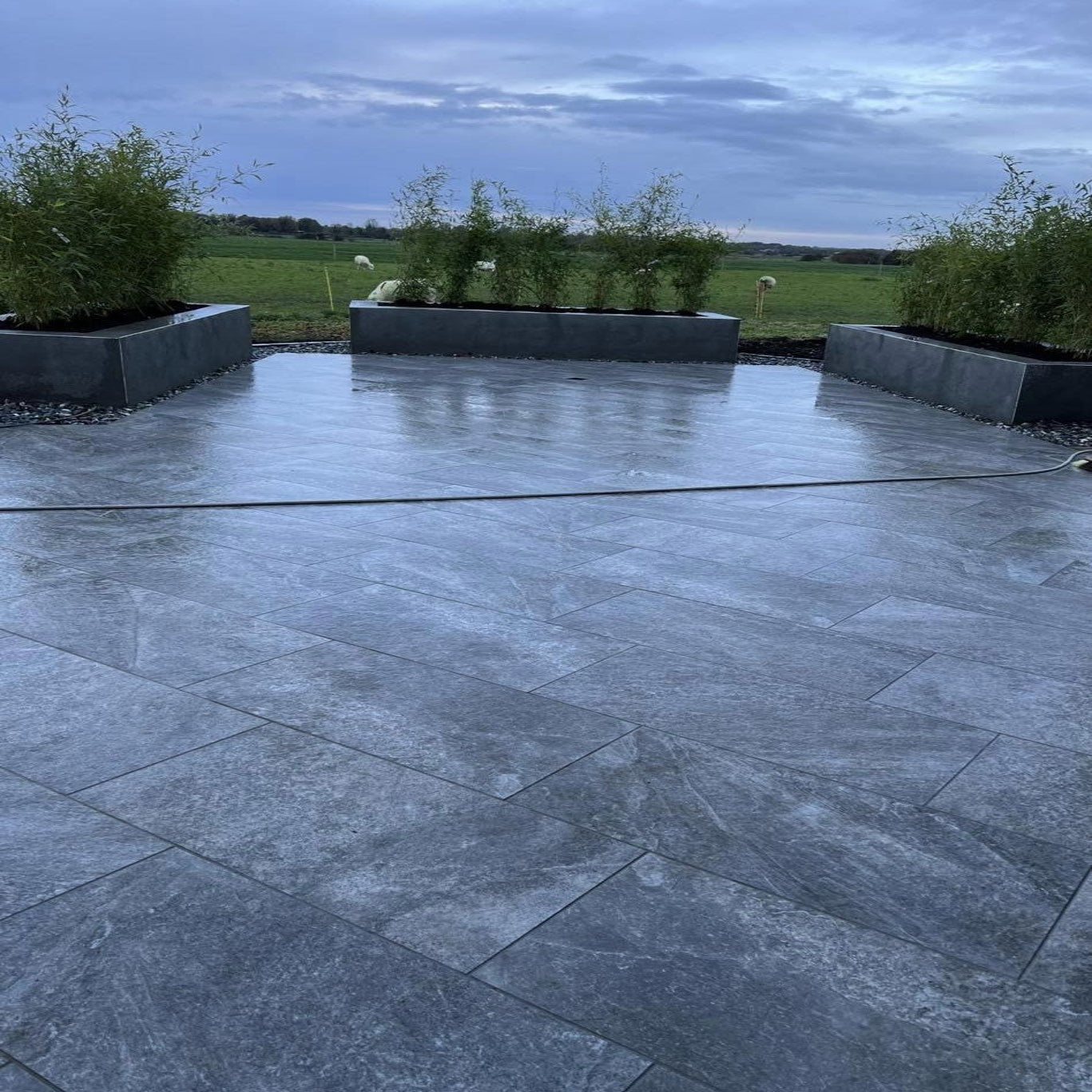 An outdoor installation of dark Twice Qz porcelain paving with plants in the background.