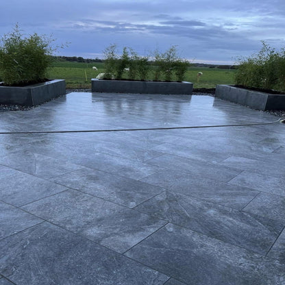An outdoor installation of dark Twice Qz porcelain paving with plants in the background.