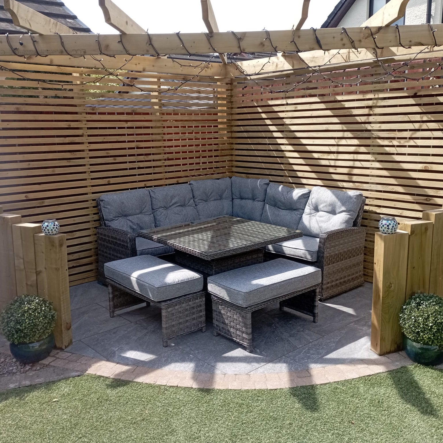 Small patio area with wooden pergola and wicker garden furniture. Paving underneath is Dark Twice Qz Range Porcelain Paving Tiles. 