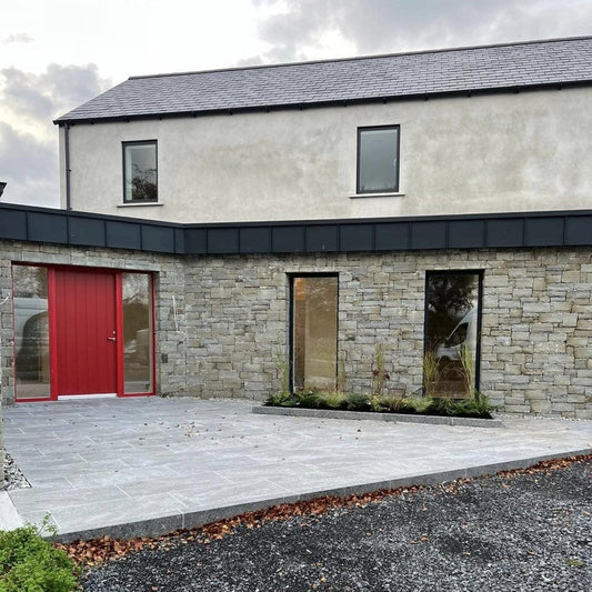 Contemporary patio outside new build with stone façade and red door. Paving is Dark Twice Qz Range Porcelain Paving Tiles. 