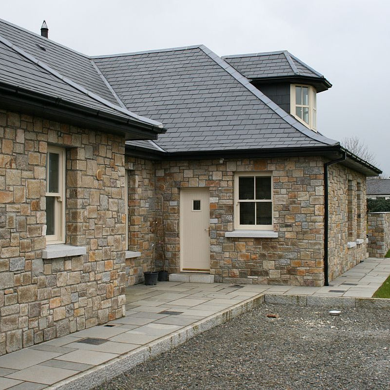 Stone house cladded in Donegal Granite Machined building stone and cream doors and windows. 