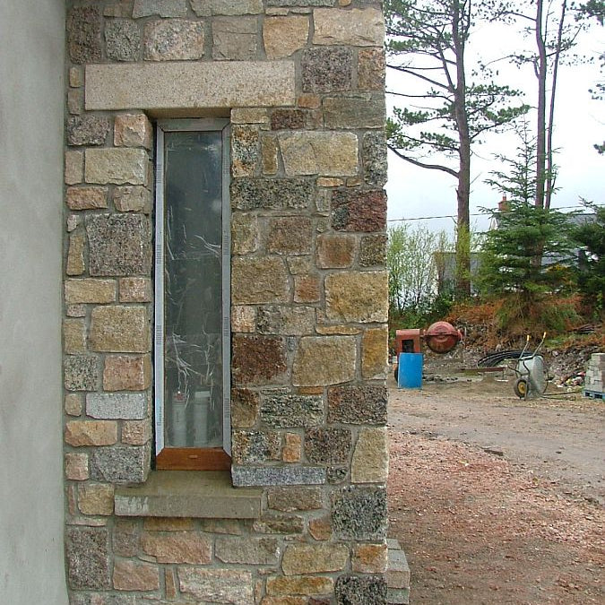 Close up of a window surrounded by Donegal Granite Building stone and gold granite lintel above the window. 