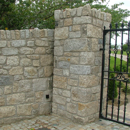 Stone wall in Donegal Granite with a black metal gate in a garden setting