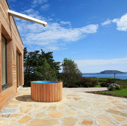 Wooden hot tub on a stone patio finished in Donegal Quartzite Crazy Paving with a scenic view of water and sky.