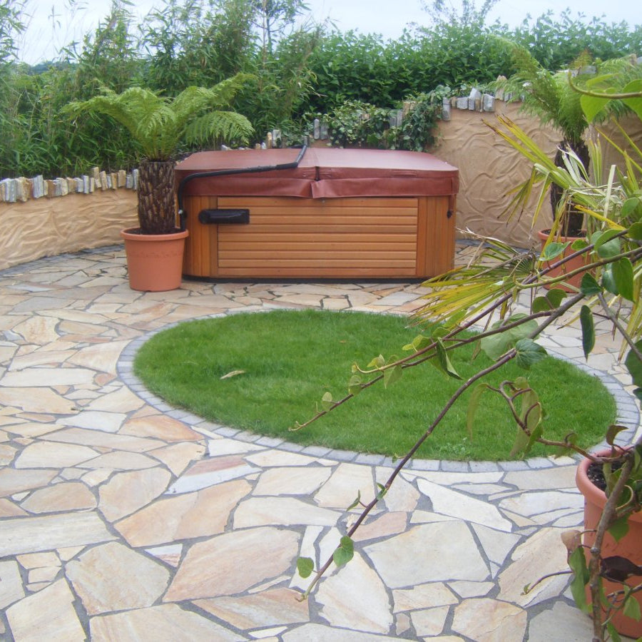 Patio area with hot tub and circular patch of grass in the centre. Paving is Donegal Quartzite Crazy Paving.  