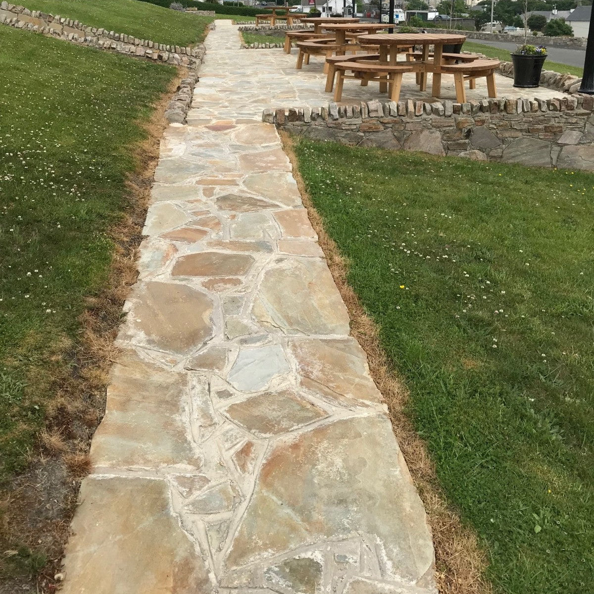 Stone pathway finished in Donegal Quartzite Crazy Paving leading to a picnic area with tables and chairs, surrounded by grass.