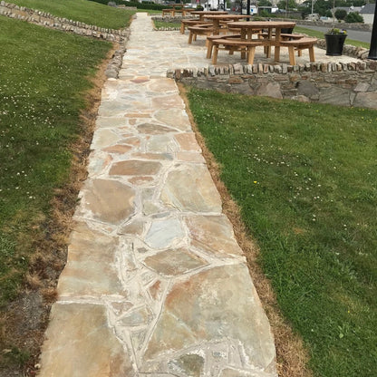 Stone pathway finished in Donegal Quartzite Crazy Paving leading to a picnic area with tables and chairs, surrounded by grass.