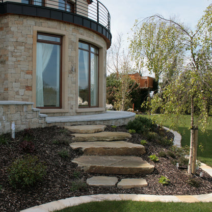 Stone steps leading up to a house with stone facade and large windows.