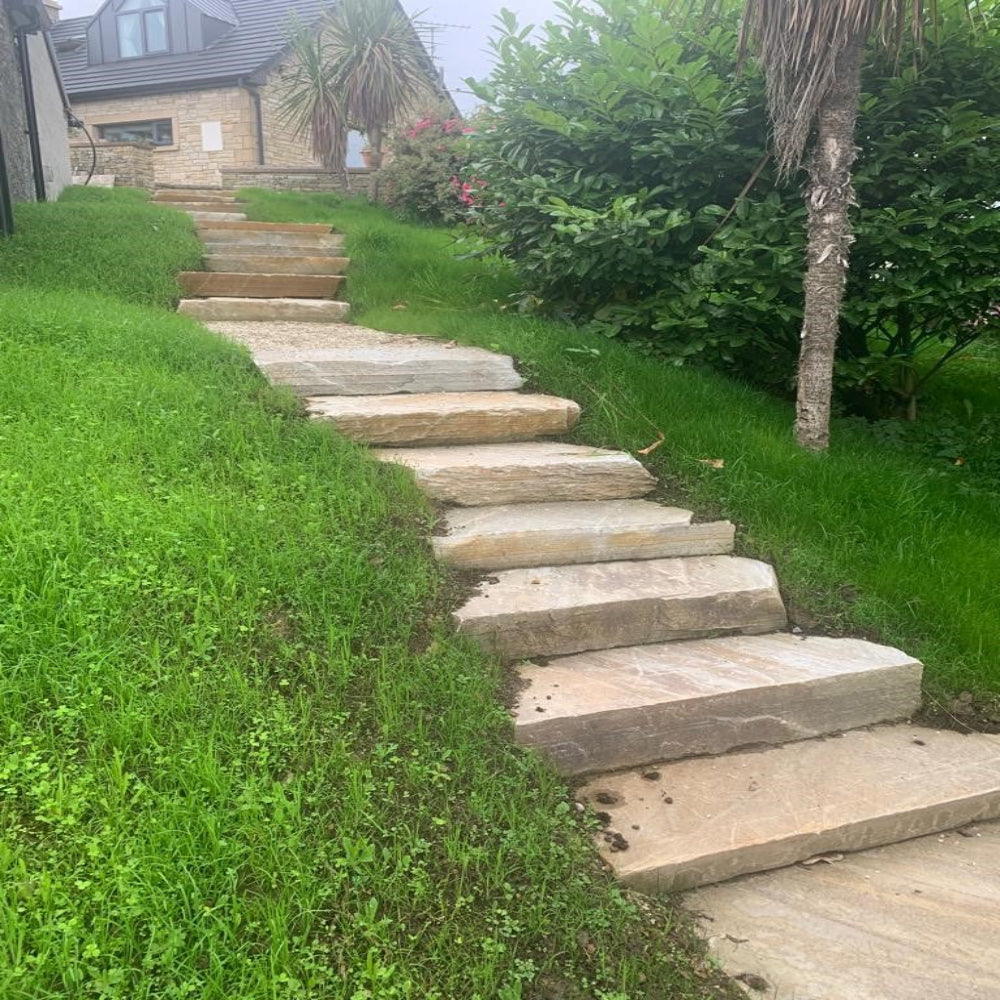 Stone steps leading up a grassy hillside with a house in the background