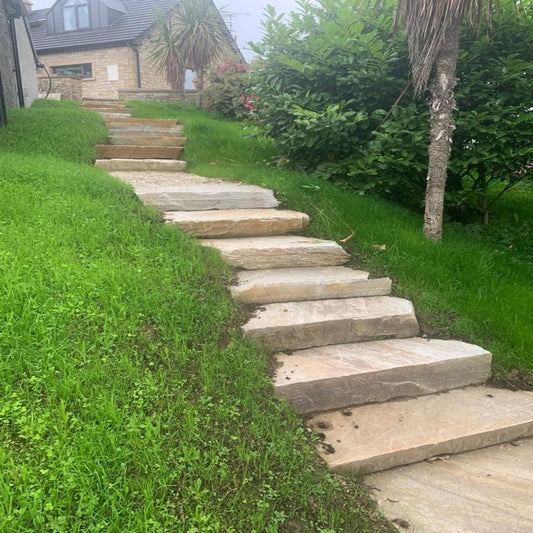 Stone steps leading up a grassy hillside with a house in the background