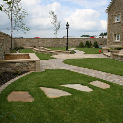 Paved pathway leading to a large stone house with grassy area and trees in the background. Garden features Donegal Quartzite Stepping Stones. 