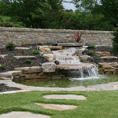 Garden with a stone wall, pond, and waterfall feature. Garden features Donegal Quartzite Stepping Stones in the foreground. 