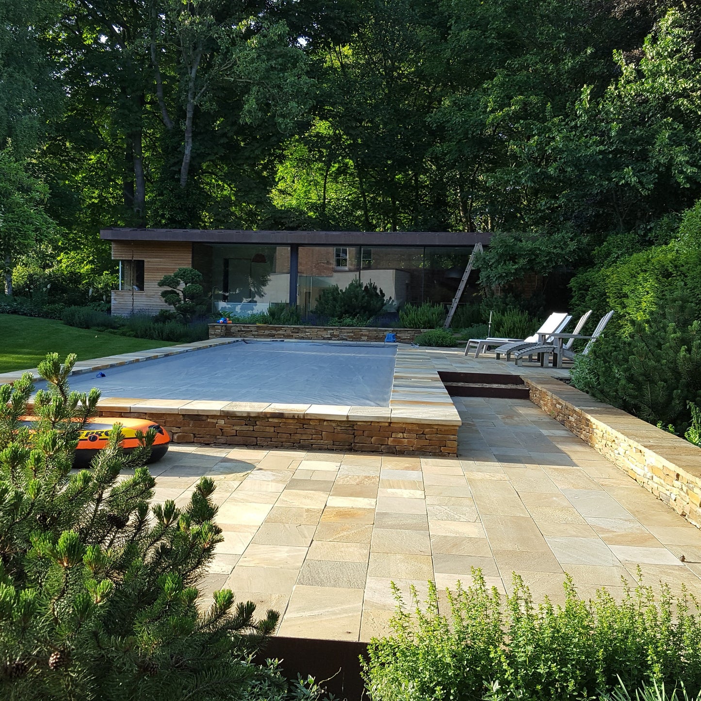 Swimming pool in a backyard surrounded by trees and greenery. Pool and garden walls completed using Donegal Quartzite Wall Capping. 