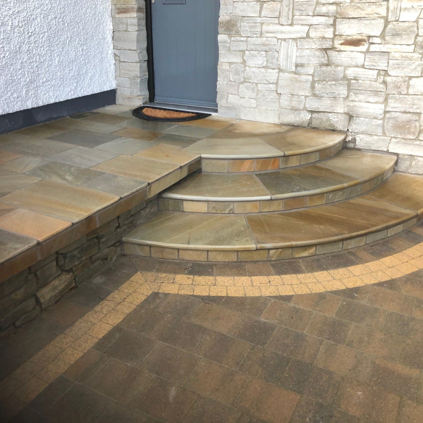 Stone steps leading up to a door with a stone wall background. Raised patio completed with Donegal Quartzite Wall Capping. 