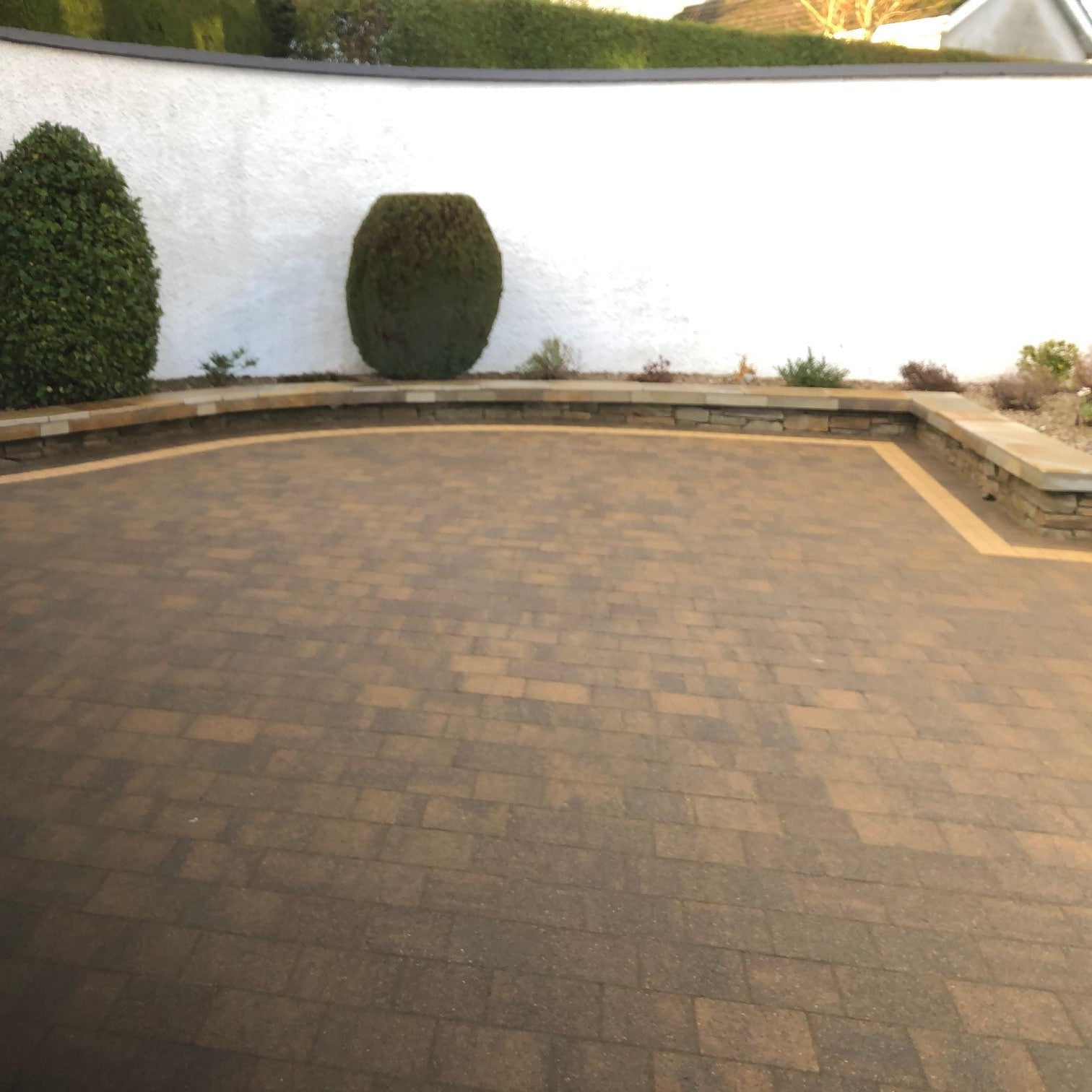 Paved driveway with a white wall and green shrubs in the background. Low  stone wall features Donegal Quartzite Wall Capping. 