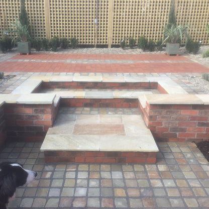 Outdoor patio with brick and stone seating area, dog in foreground. Walls completed using Donegal Quartzite Wall Capping. 