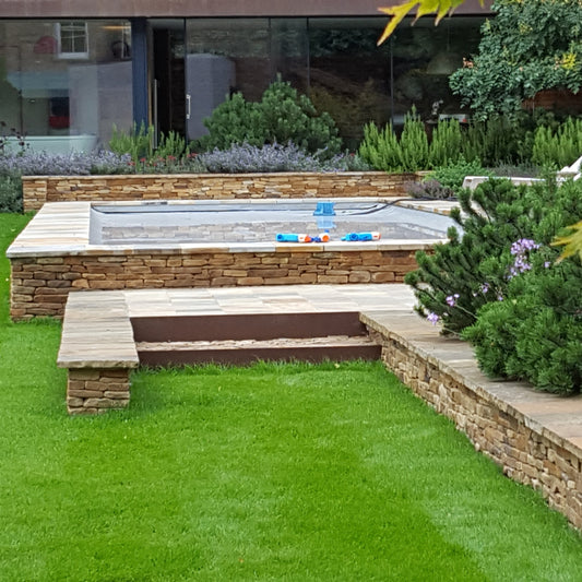 Garden with a pool, green grass, and decorative plants. Pool and garden wall are completed using Donegal Quartzite Wall Capping. 