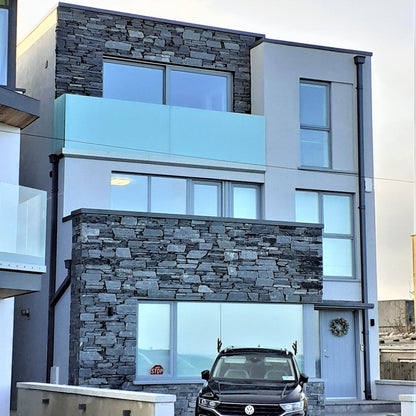 Modern house with stone facade in Donegal Slate Rubble and glass windows, featuring a black SUV in front.