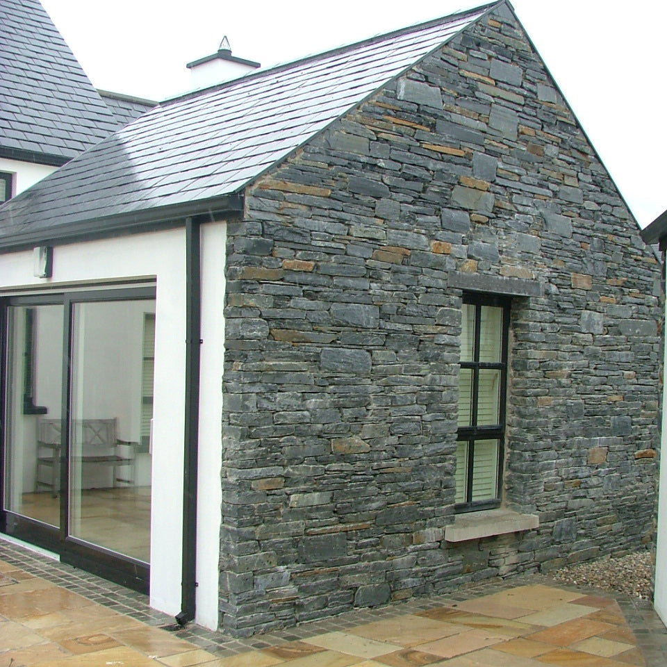 Modern house exterior with stone facade in Donegal Slate Rubble and glass sliding door. 
