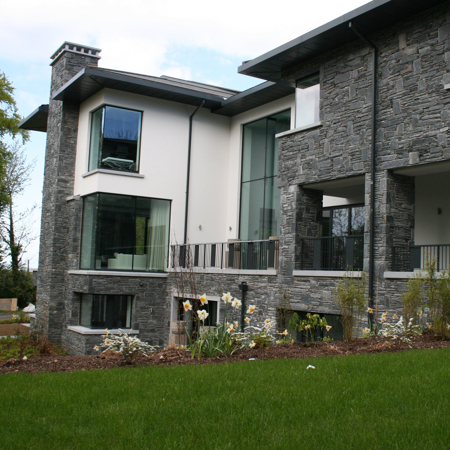 Modern house with stone facade in Donegal Slate Rubble and large windows, surrounded by greenery.