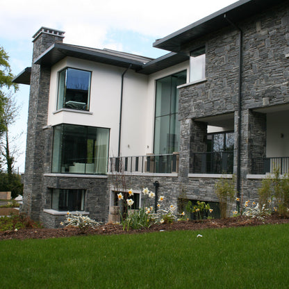 Modern house with stone facade in Donegal Slate Rubble and large windows, surrounded by greenery.