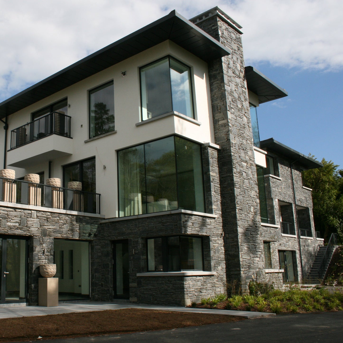 Modern house with stone façade in Donegal Slate Rubble surrounded by trees on a cloudy day.