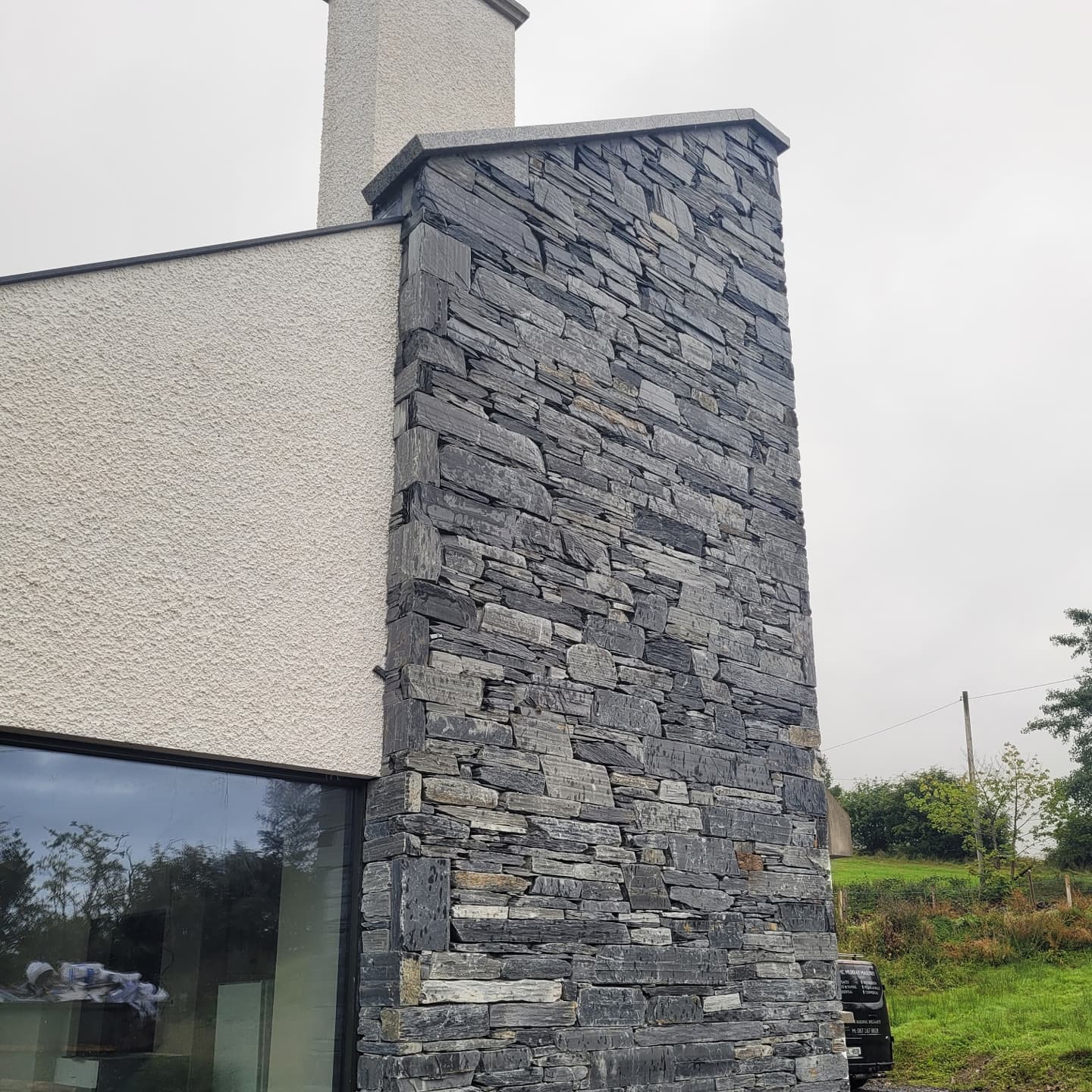 Stone chimney in Donegal Slate Rubble on a modern building exterior with a cloudy sky.