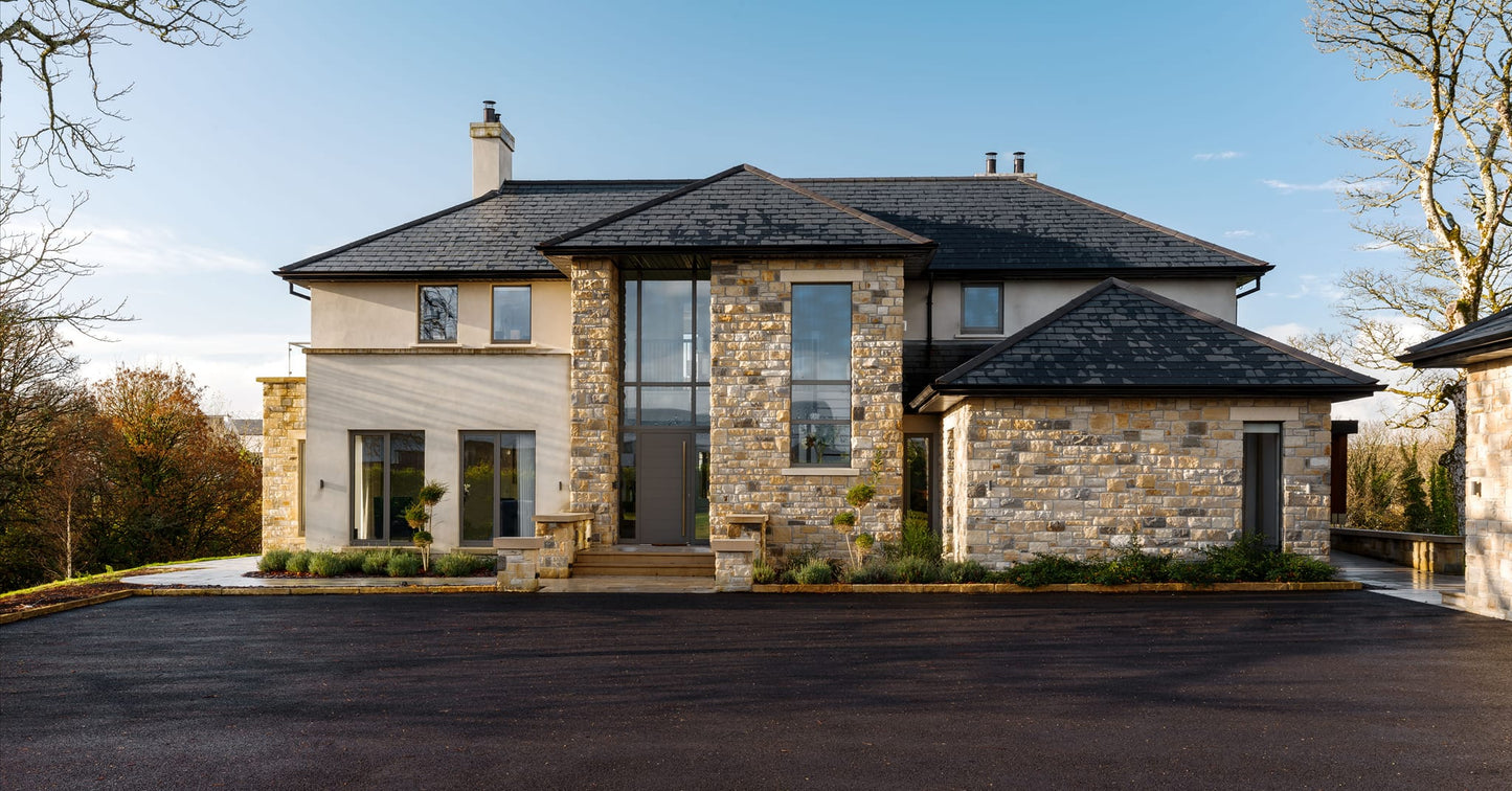 Modern stone house with large windows and a driveway. Stonework is Dunhill Blend Sandstone Machined. 