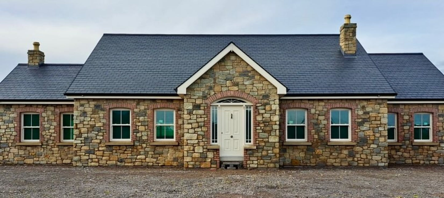 Stone house completed in Dunhill Blend Sandstone with a tumbled finish and red brick detail around the windows and door. 