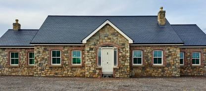 Stone house completed in Dunhill Blend Sandstone with a tumbled finish and red brick detail around the windows and door. 