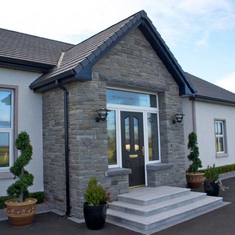 Modern house with stone facade and black door, surrounded by potted plants. Stone is Dust Grey Sandstone. 