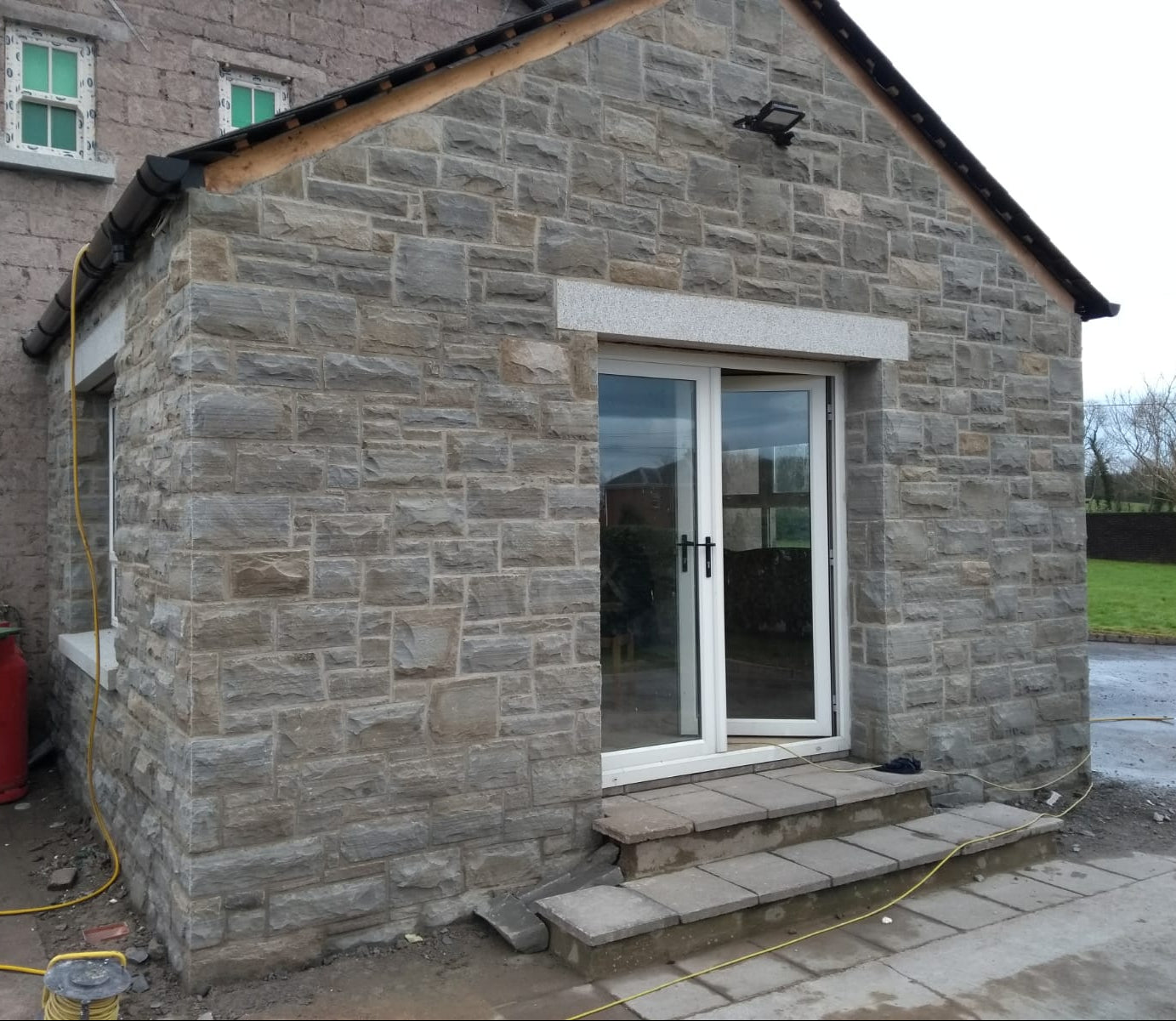 Stone building with patio glass door and steps leading up to it. Stone is Dust Grey Sandstone - Machined. 