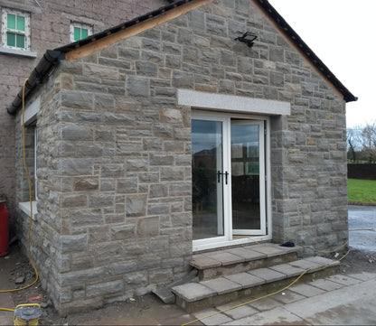 Stone building with patio glass door and steps leading up to it. Stone is Dust Grey Sandstone - Machined. 