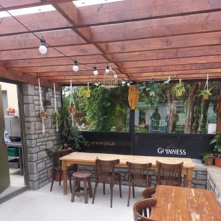 Outdoor seating area with wooden tables and chairs under a wooden pergola, featuring a Guinness advertisement in the background. Stonework is Dusty Grey Sandstone Stoneer Cladding.