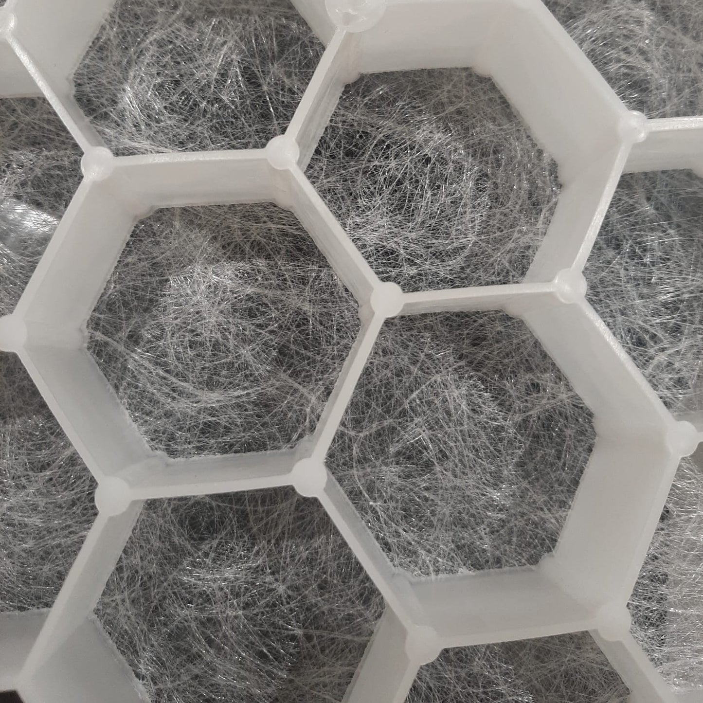 White hexagonal grid structure containing gray fibrous material, shown in a close-up view.