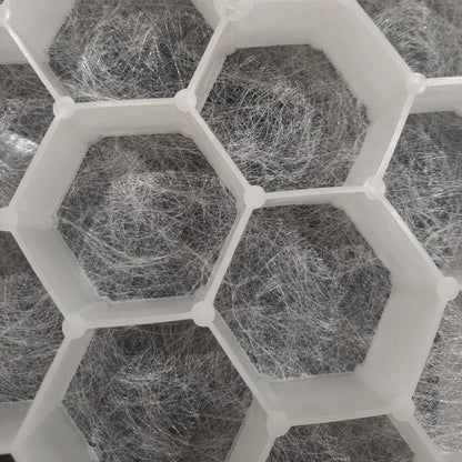 White hexagonal grid structure containing gray fibrous material, shown in a close-up view.