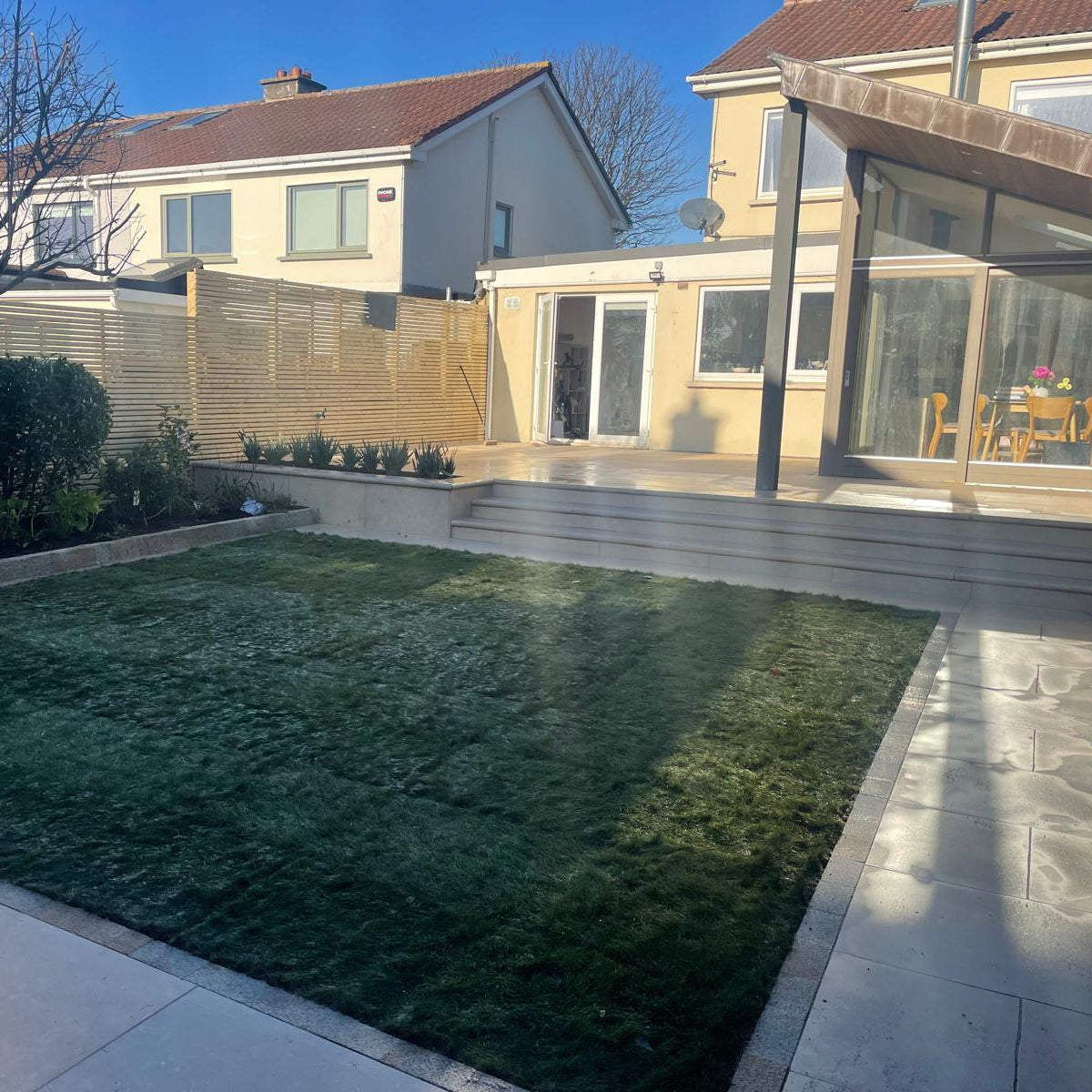 Modern house extension with patio area leading down to garden. Grass is bordered by Egyptian Limestone Paving Setts. 