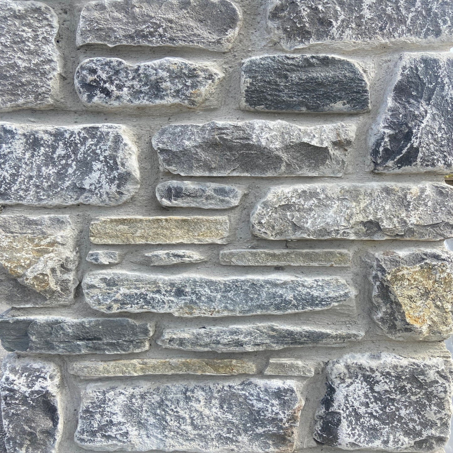 A close-up image of a wall constructed from Fieldstone Blend stones, showing a variety of grey and brown shades with a tumbled finish.