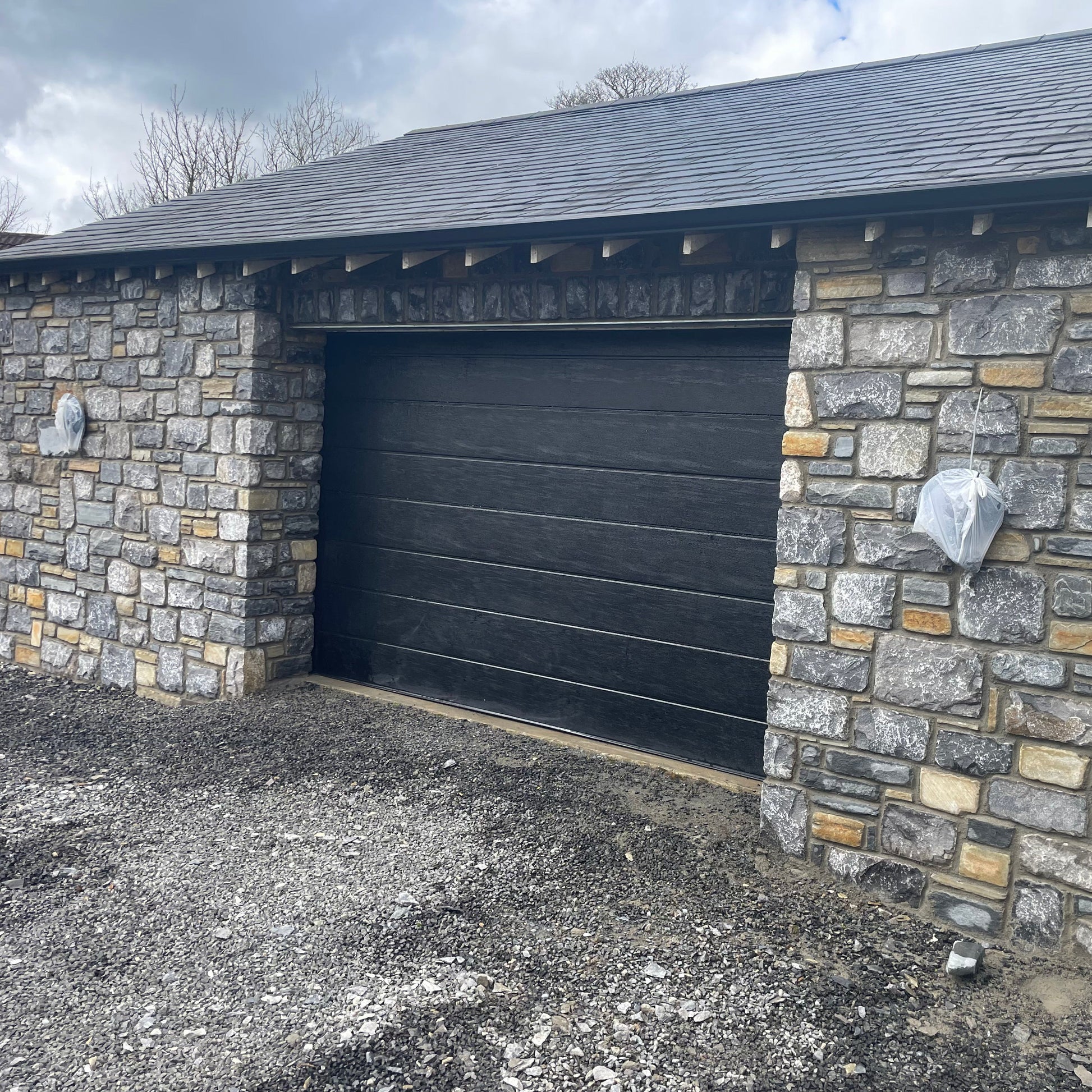 New build garage with a black door and a stone façade in Fieldstone Blend with a tumbled finish. 