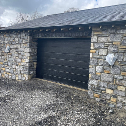 New build garage with a black door and a stone façade in Fieldstone Blend with a tumbled finish. 