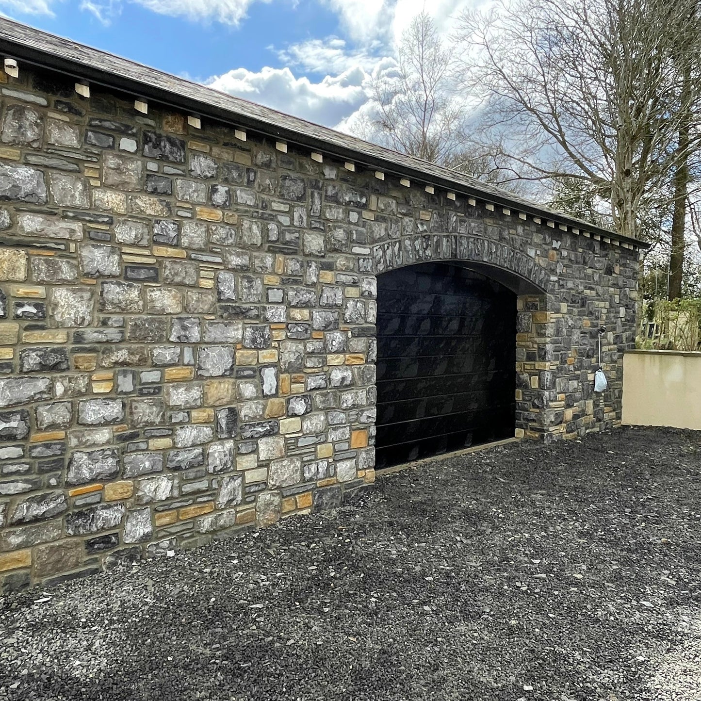 New build garage with a black door and a stone façade in Fieldstone Blend. 