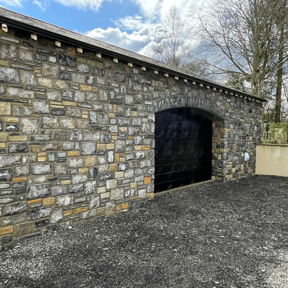New build garage with a black door and a stone façade in Fieldstone Blend. 