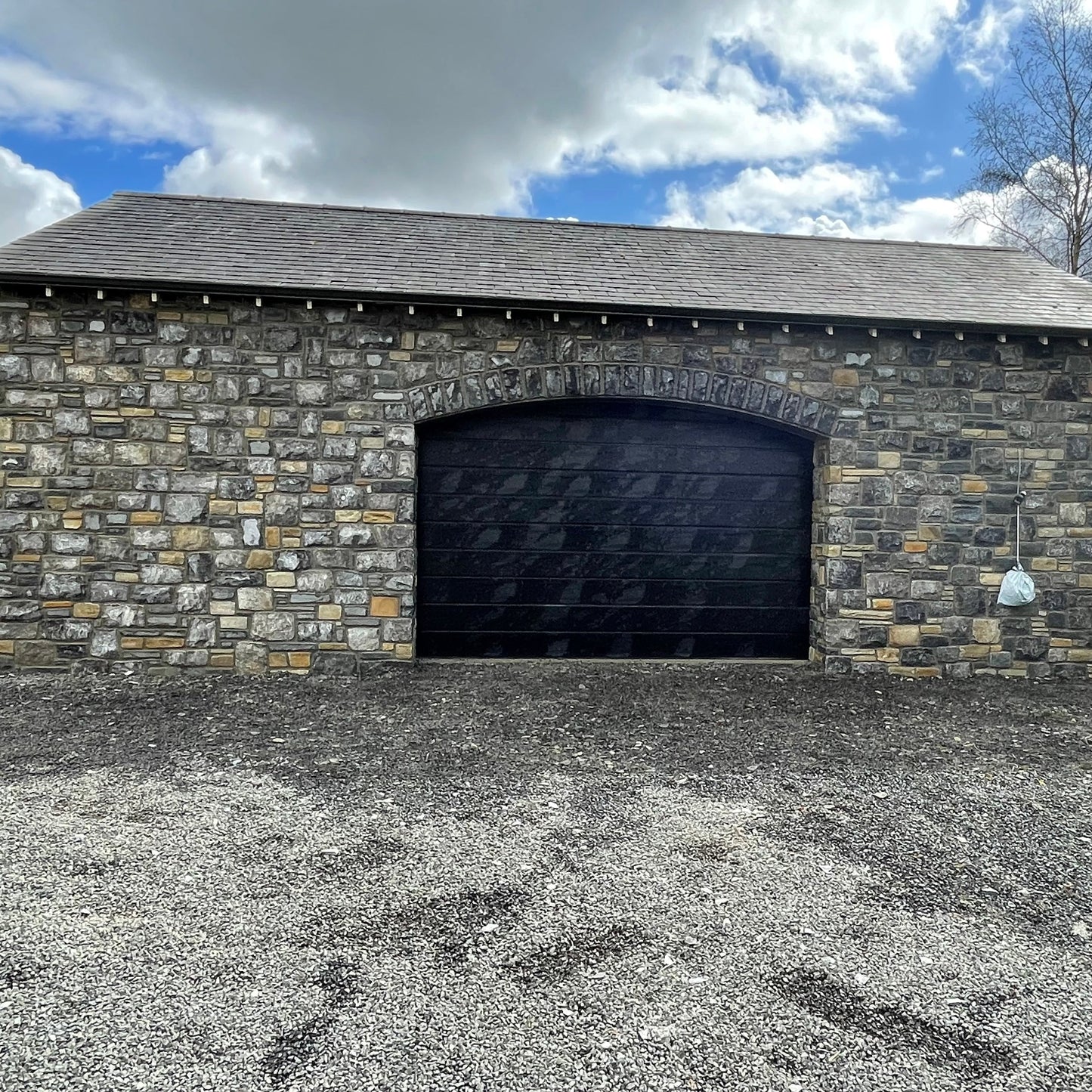 New build garage with a black door and a stone façade in Fieldstone Blend. 