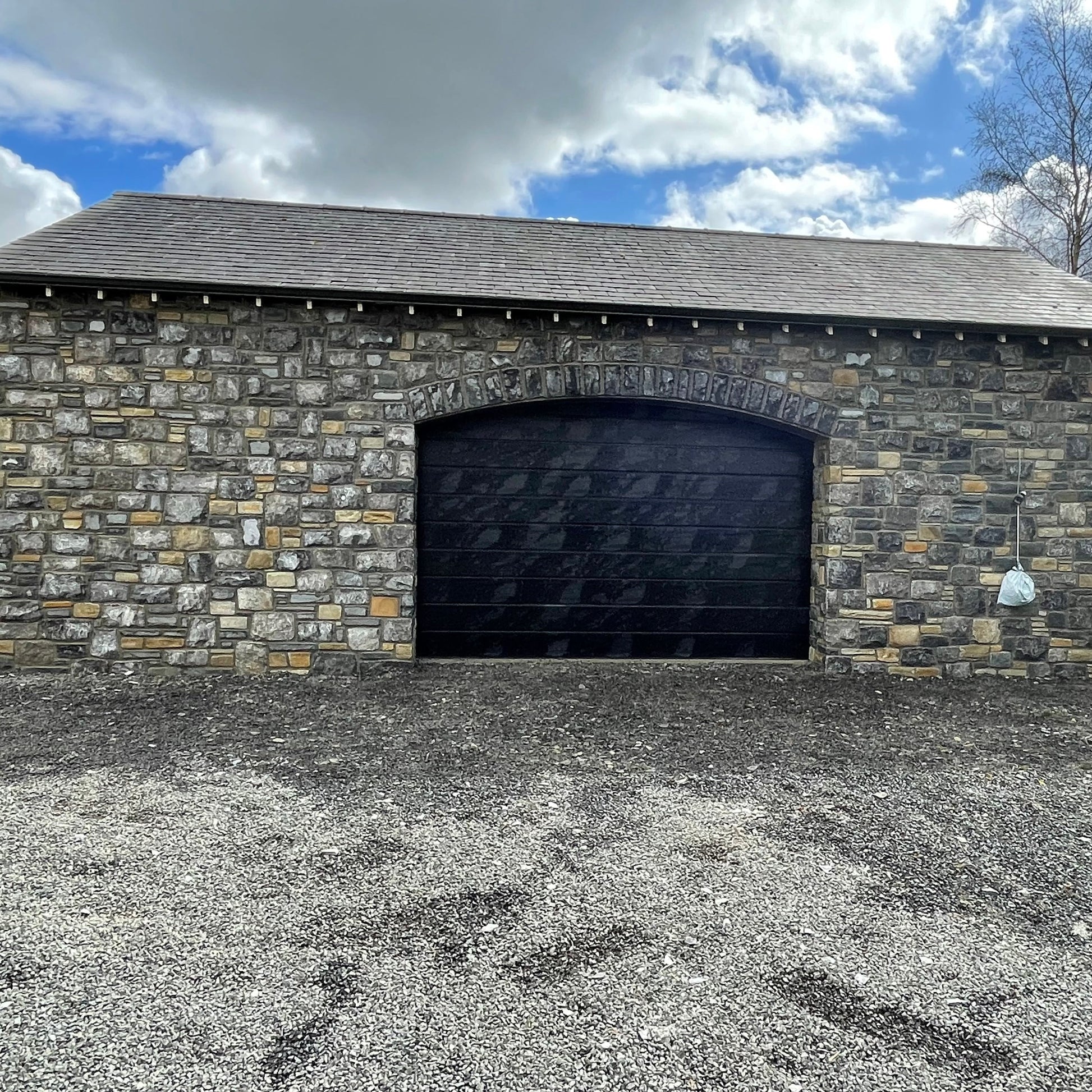 New build garage with a black door and a stone façade in Fieldstone Blend. 